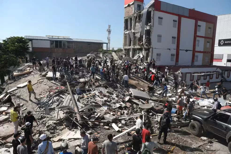Vista aérea de um quarteirão destruído com dezenas de pessoas a trabalhar sobre os escombros